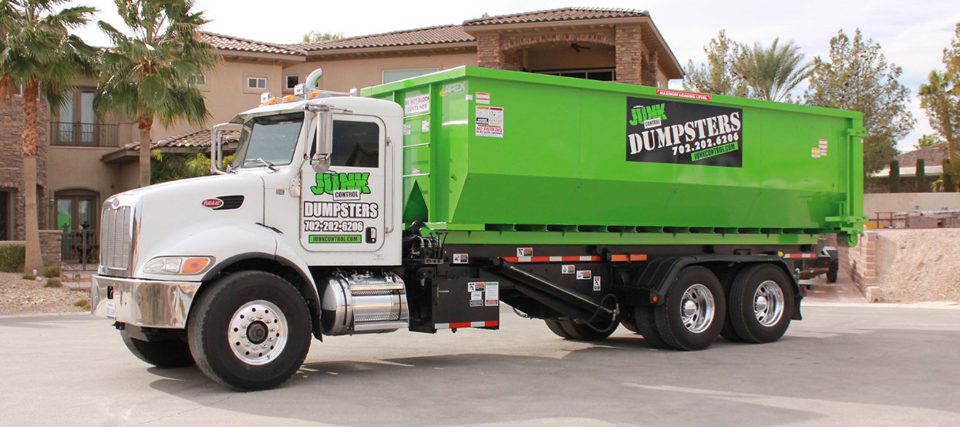 A Junk Control roll-off dumpster truck parked in front of a house